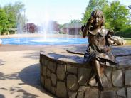Statue of girl sitting in front of splash pad